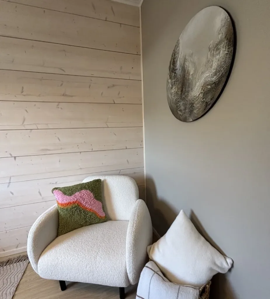 Nojatuoli, taulu ja tyynyjä vaaleissa sävyissä